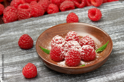 A dessert of fresh ripe raspberries and powdered sugar closeup on wooden plate on a background  Board.