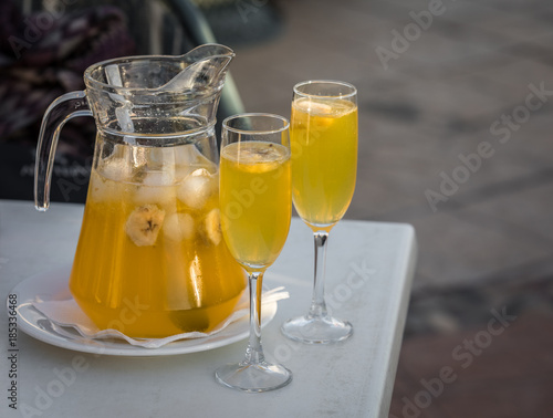 Yellow champagne sangria served in a mug with two glasses