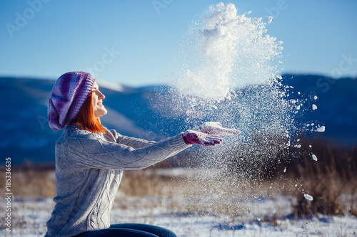 Winter portrait of young beautiful brunette woman wearing knitted snood covered in snow. Snowing winter beauty fashion concept.