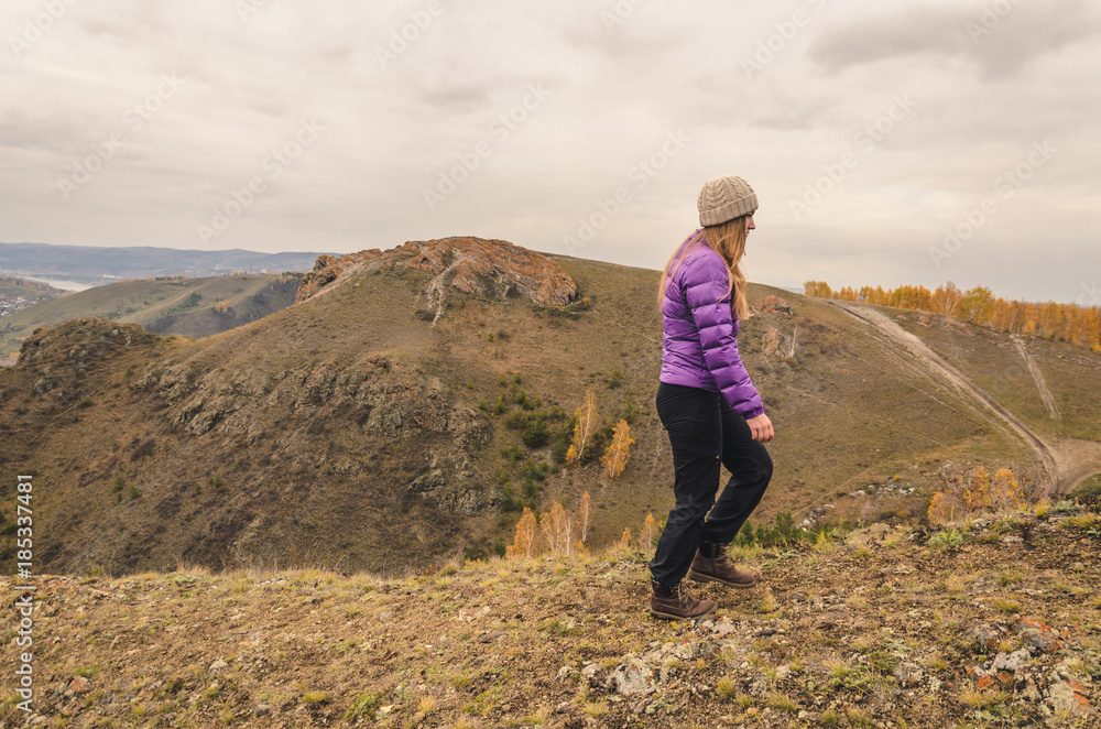 A girl in a lilac jacket walks in the mountains, an autumn forest with a cloudy dayю. Free space for text