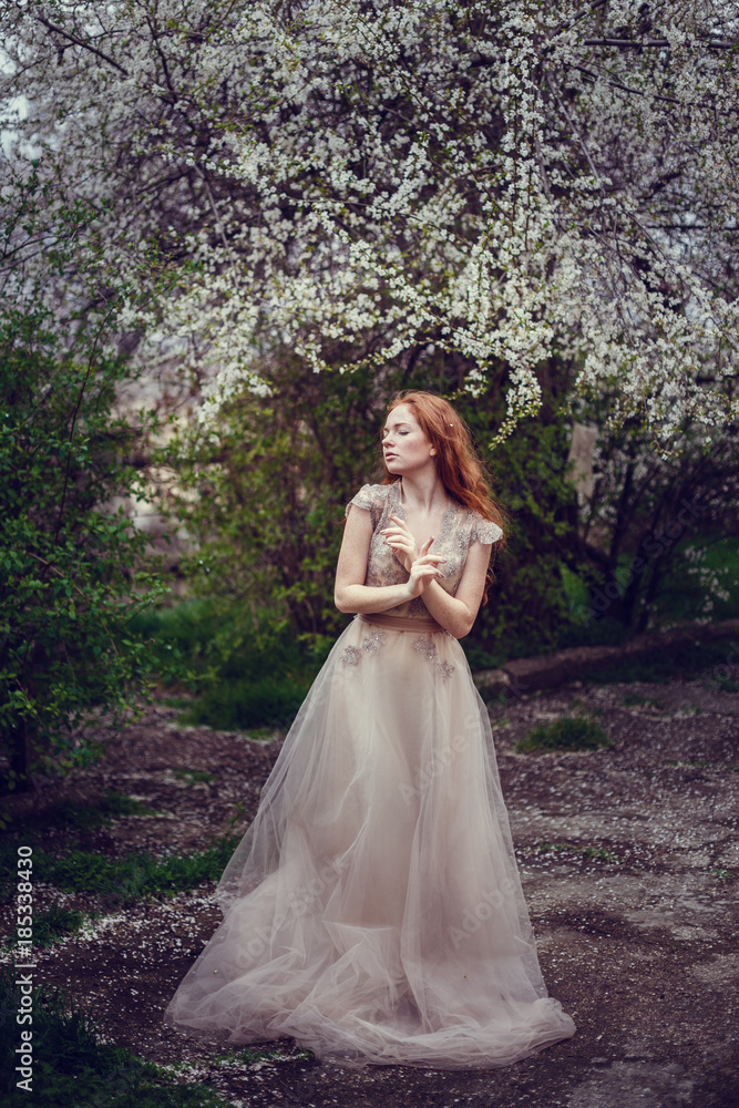 Beautiful happy young woman with red hair enjoying smell in a flowering spring garden