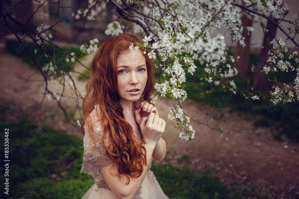 Beautiful happy young woman with red hair enjoying smell in a flowering spring garden Beautiful happy young woman with red hair enjoying smell in a flowering spring garden