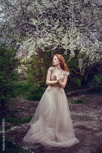 Beautiful happy young woman with red hair enjoying smell in a flowering spring garden © selenit