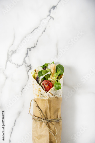 Fresh tortilla wrap on a marble pattern tabletop tied round with brown paper and string. Top view shot. Gourmet conception.