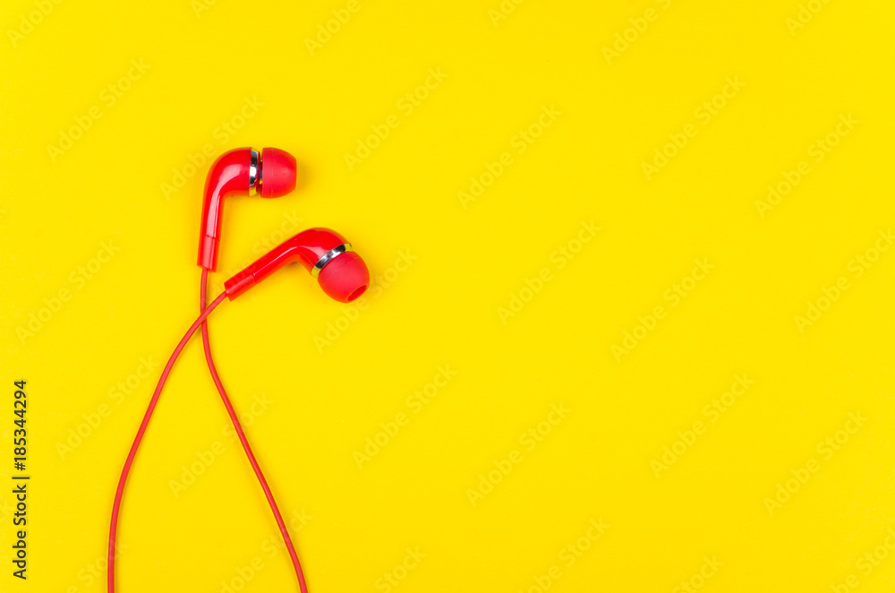 Bright red earbud headphones isolated on a bright yellow background with copy space on the right for your text (minimal concept, top view) Bright red earbud headphones isolated on a bright yellow background with copy space on the right for your text (minimal concept, top view)