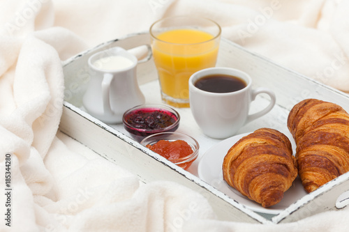 Freshly baked croissant, orange juice, jam, cup of black coffee on white wooden tray on plaid. Homemade cookie. Fresh pastries for breakfast. Delicious dessert. Closeup photography. Horizontal banner