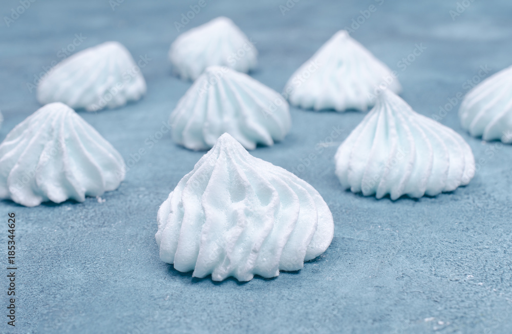 Rows of freshly baked meringue cookies on a light gray-blue concrete or marble background (shallow DOF, selective focus)