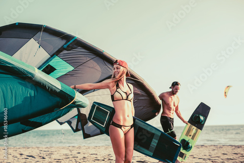 Pretty smiling Caucasian woman kitesurfer enjoying summertime on sandy beach with her boyfriend.
