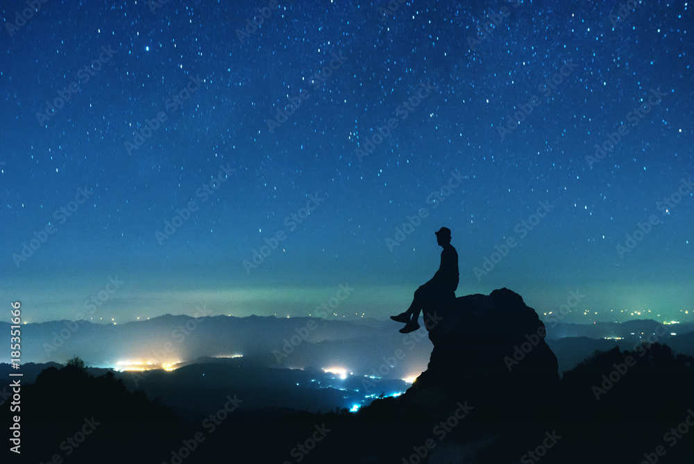 Man sits on big rock on night sky background
