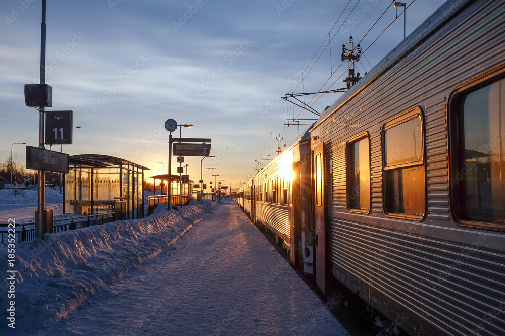 A snow-covered railway stop with a train and the sun rising