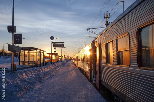 A snow-covered railway stop with a train and the sun rising