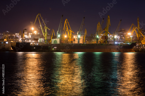 Vessel dry cargo on loading, unloading in port at night time. Bulker in port.