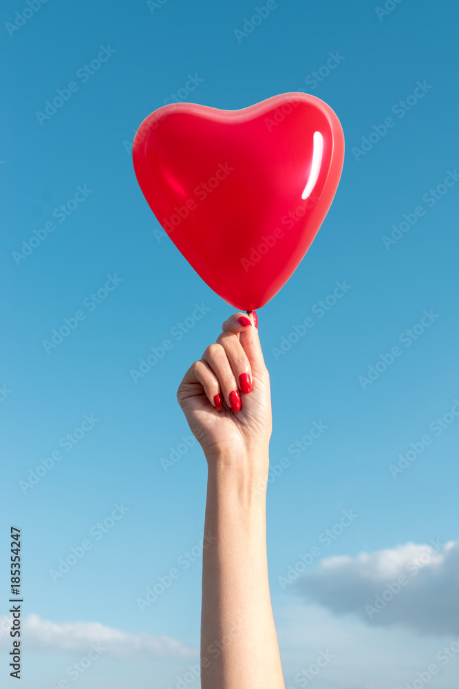 Fototapeta premium Womans hand with heart shaped balloon on background of sky.