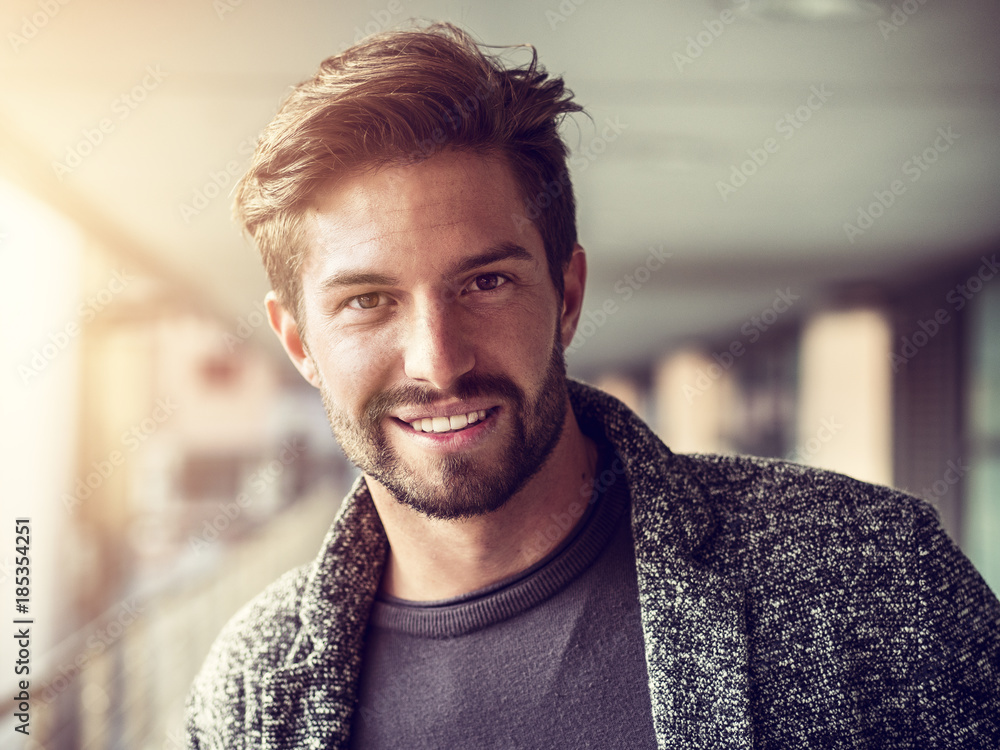 One handsome young man in urban setting in European city, standing, smiling and looking at camera - obrazy, fototapety, plakaty 