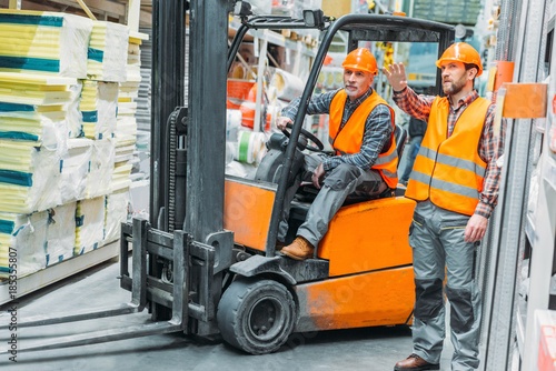 worker and his senior colleague working with forklift machine in storage photo