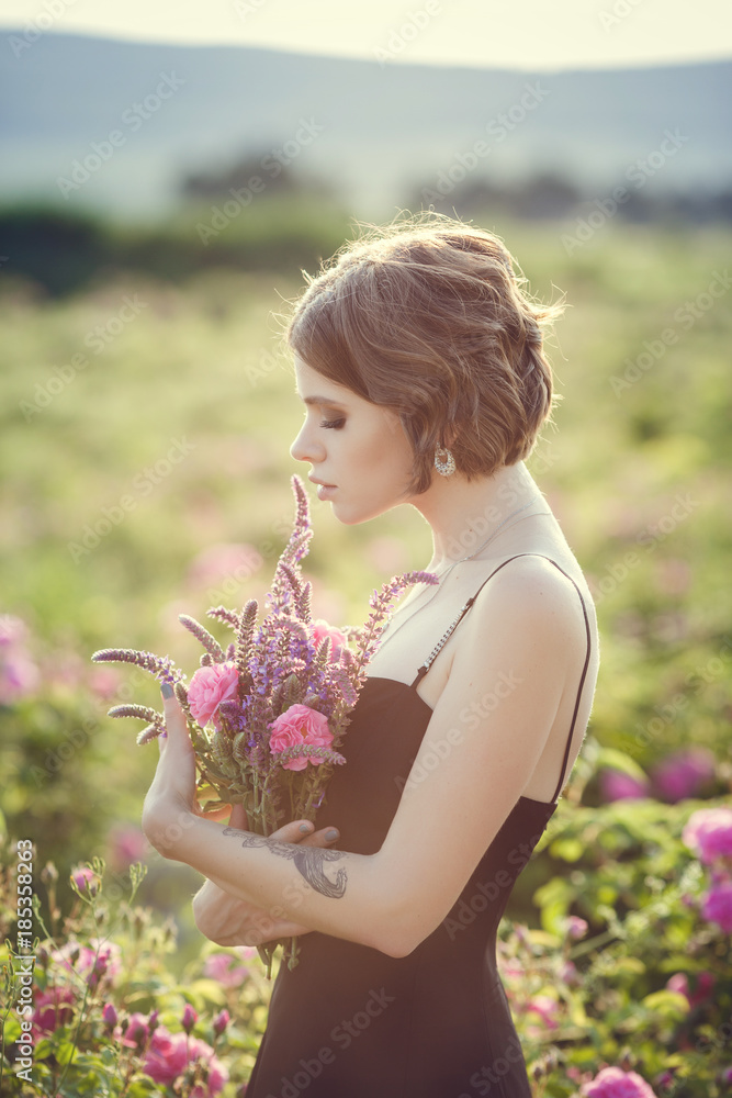 Fototapeta premium Beautiful young woman in a blooming rose garden