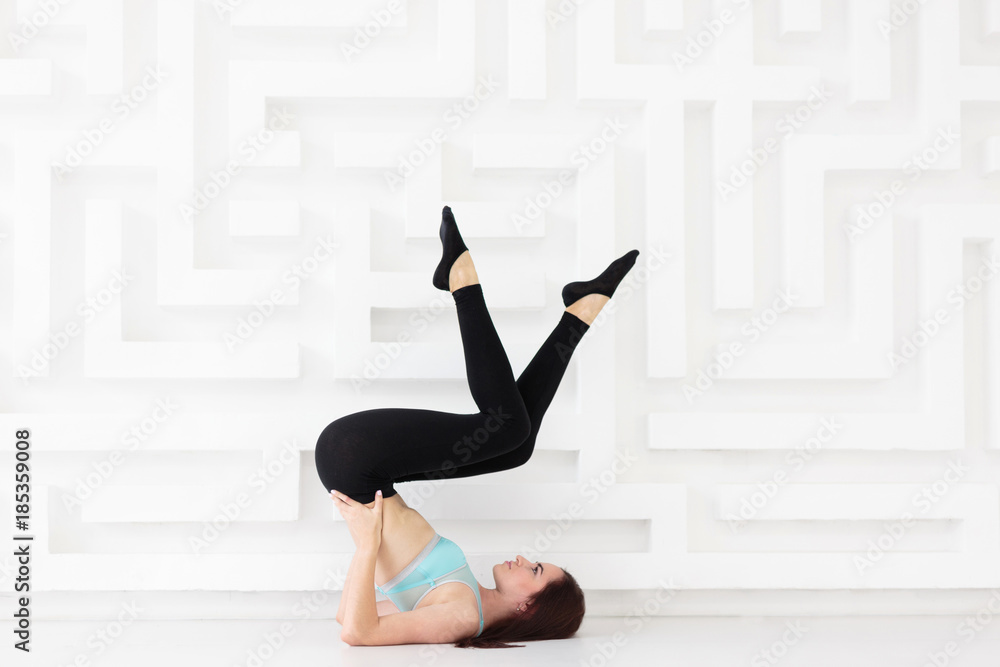 Young beautiful woman working out in studio while practicing pose with lifted legs Young beautiful woman working out in studio while practicing pose with lifted legs