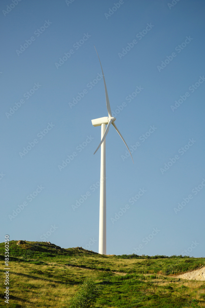 Wind turbine on hill generating electricity over a blue sky background. Clean and ecological energy production concept. Wind turbine on hill generating electricity over a blue sky background. Clean and ecological energy production concept.