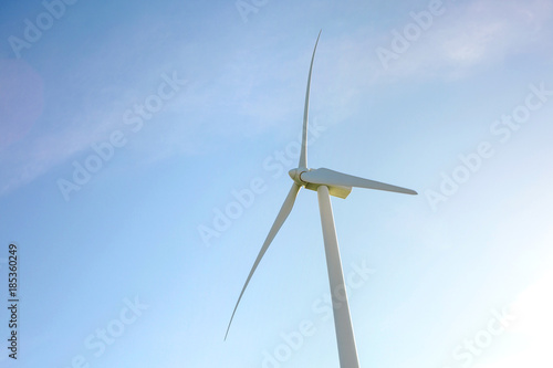 Closeup of windmill turbine and blades generating electricity over a blue sky background. Clean and ecological energy production concept. © David Pereiras
