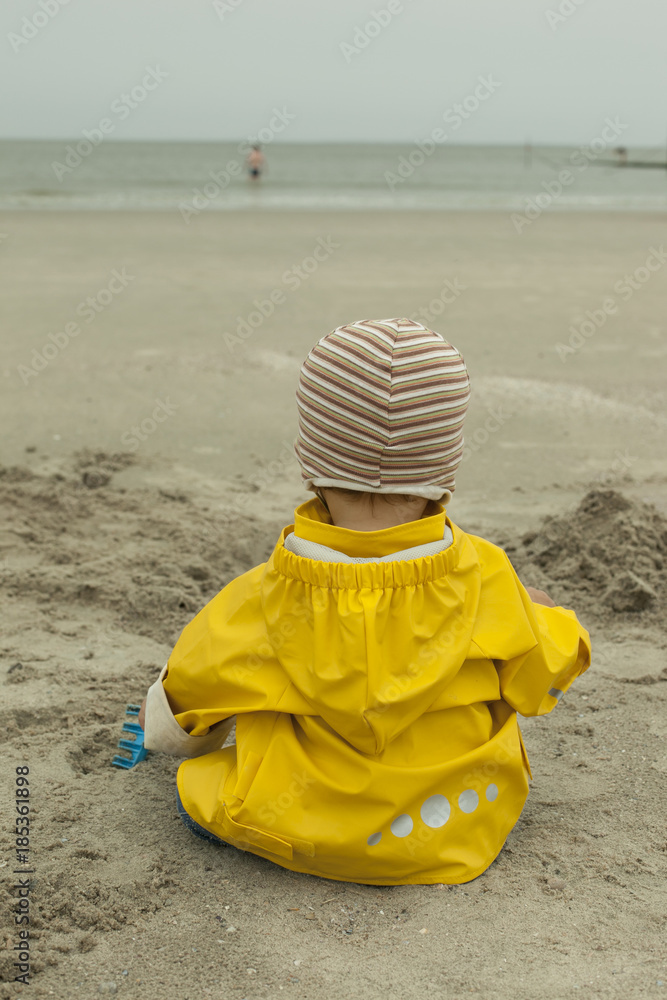 baby boy in yellow rain coat plays on the beach baby boy in yellow rain coat plays on the beach