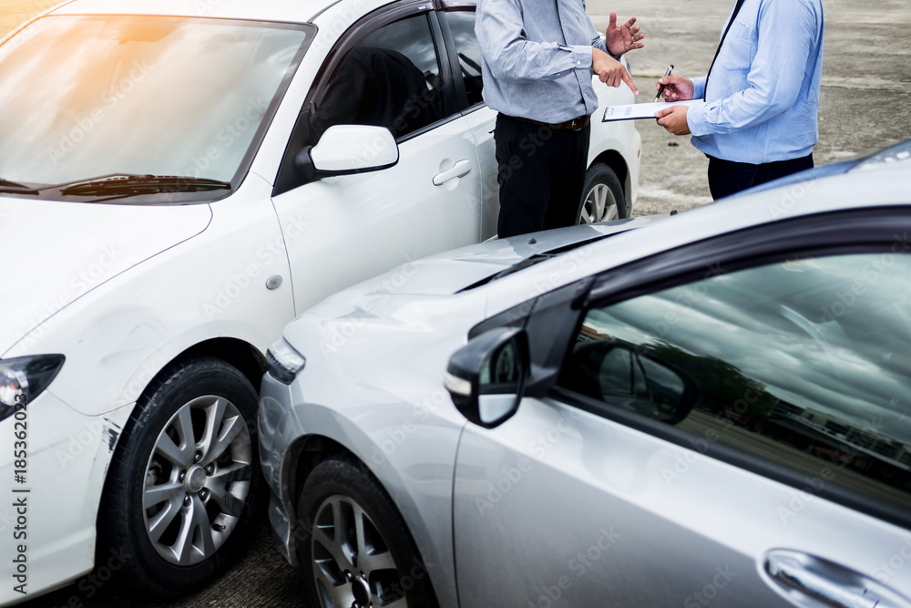 Insurance agent writing on clipboard while examining car after accident claim being assessed and processed. Insurance agent writing on clipboard while examining car after accident claim being assessed and processed.