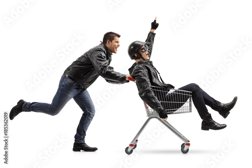 Biker pushing a shopping cart with another biker holding his finger up riding inside