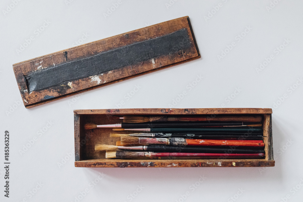 Directly above shot of paintbrushes in wooden case over white background Directly above shot of paintbrushes in wooden case over white background
