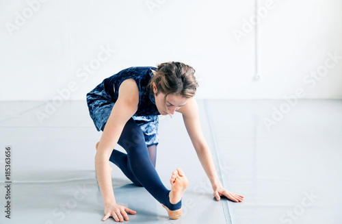 Young female performer dressed in blue velvet dress practicing contemporary dance elements in white spacious loft. Natural lighting. Horizontal composition with copy space.