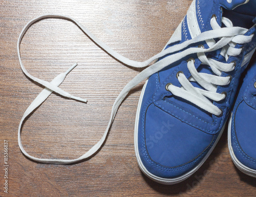 White Leather Shoes with Untied Laces in Heart Form on Wooden Floor
