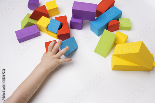 Childrens hand holds multi-colored toy building blocks on white background photo
