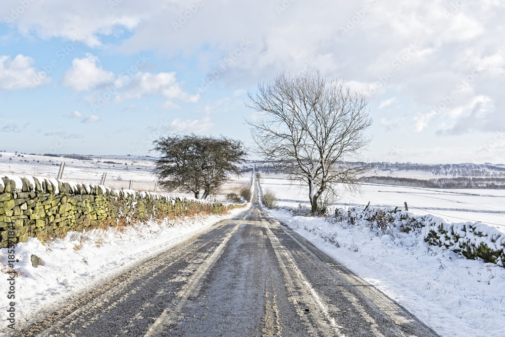 Down a long, straight and narrow road, between snow covered moorland in the Peak District.