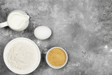 Ingredients for pastries - flour, eggs, butter, milk, sugar on a gray background. Top view, copy space. Food background