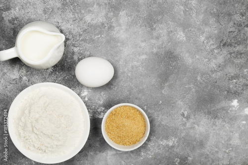 Ingredients for pastries - flour, eggs, butter, milk, sugar on a gray background. Top view, copy space. Food background