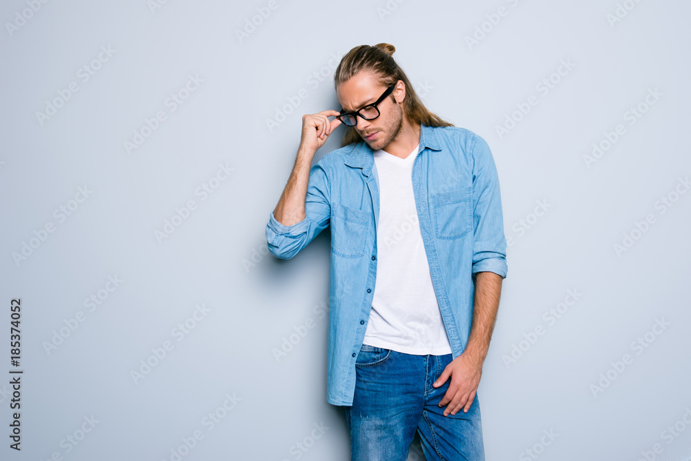 Portrait with copy space of fashionable, stunning, successful guy with hairstyle, posing, holding eyelet of glasses on face with fingers, looking down with serious expression over grey background Portrait with copy space of fashionable, stunning, successful guy with hairstyle, posing, holding eyelet of glasses on face with fingers, looking down with serious expression over grey background