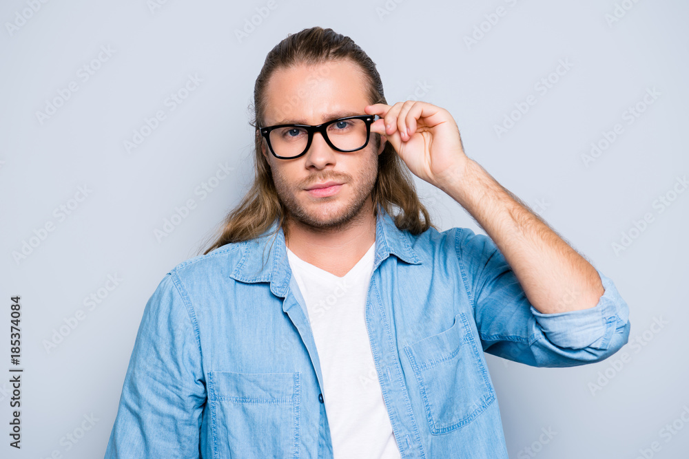 Close up portrait of stunning, successful guy with hairstyle, holding eyelet of glasses on face with fingers, looking at camera with serious expression over grey background Close up portrait of stunning, successful guy with hairstyle, holding eyelet of glasses on face with fingers, looking at camera with serious expression over grey background