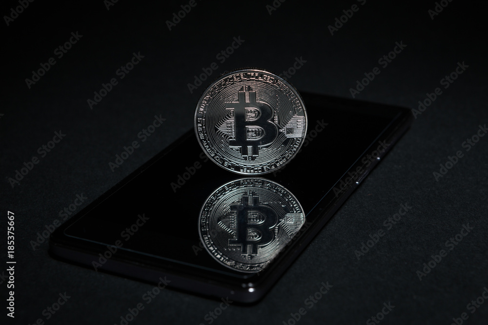 One silver metallic bitcoin on mobile phone screen One silver metallic bitcoin on mobile phone screen