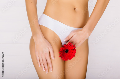 slim woman dressed in white panties, holding a red flower in her hands, close-up. Gynecology, menstruation, the concept of genital health © Peakstock