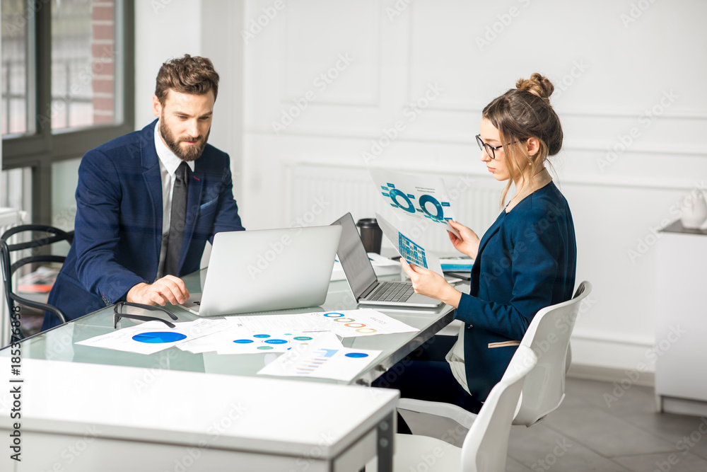 Obraz premium Marketer or analityc manager team dressed in suits working with paper charts and laptops at the white office interior