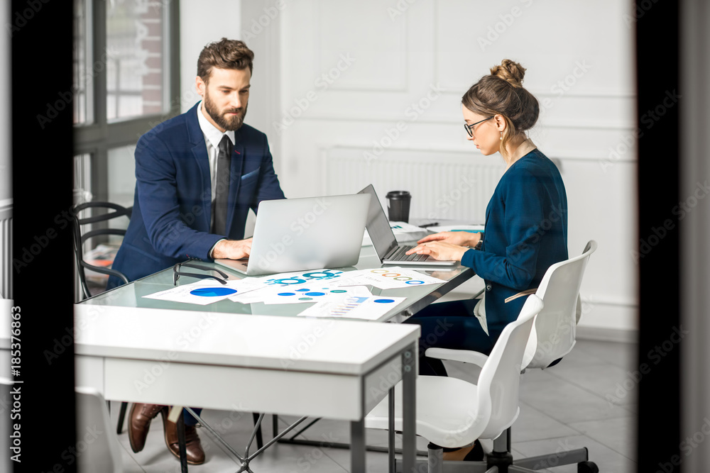 Marketer or analityc manager team dressed in suits working with paper charts and laptops at the white office interior Marketer or analityc manager team dressed in suits working with paper charts and laptops at the white office interior