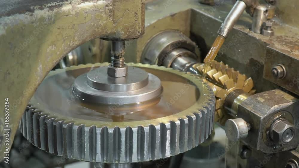 The machine on the plant, which is trenching the alluminium circle. The detail is turning anti clockwise and the cutting machine is twisting from up to down. The oil is being poured to the workpiece The machine on the plant, which is trenching the alluminium circle. The detail is turning anti clockwise and the cutting machine is twisting from up to down. The oil is being poured to the workpiece