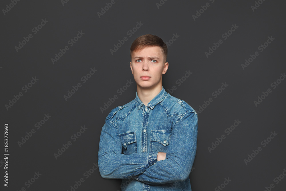 Obraz premium Portrait of young handsome man in jeans shirt looking at camera over dark grey background. Emotions and facial expressions concept.