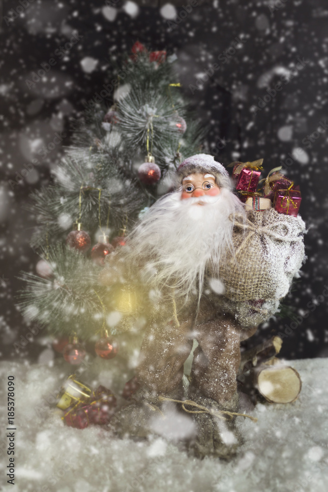 Santa Claus Outdoors Beside Christmas Tree in Snowfall Carrying Gifts to Children. Merry Christmas & New Year's Eve concept Santa Claus Outdoors Beside Christmas Tree in Snowfall Carrying Gifts to Children. Merry Christmas & New Year's Eve concept