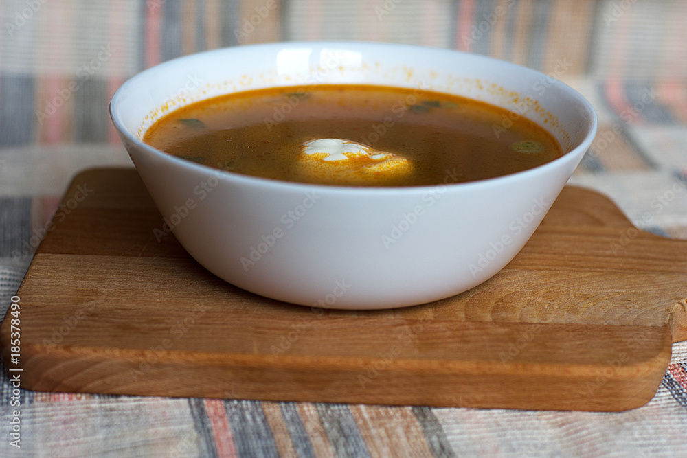 Vegetable soup with sour cream in a white bowl on a wooden stand and a towel Vegetable soup with sour cream in a white bowl on a wooden stand and a towel