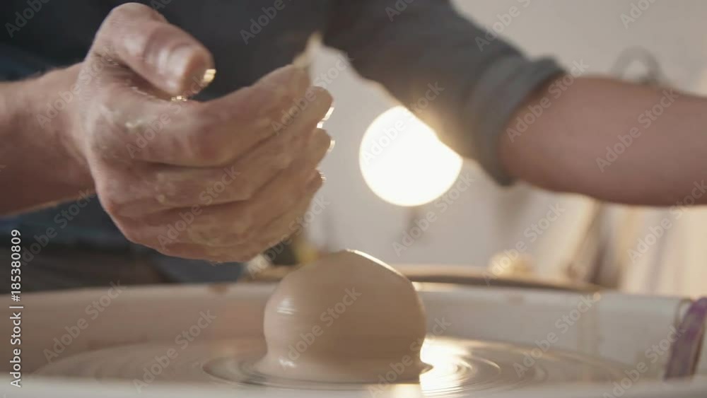 Potter at work: men's hands, stained with clay, work with a potter's wheel. Man-ceramist creates a product of light clay in studio, close-up. Crafting, custom-made products: ceramics and clay products Potter at work: men's hands, stained with clay, work with a potter's wheel. Man-ceramist creates a product of light clay in studio, close-up. Crafting, custom-made products: ceramics and clay products