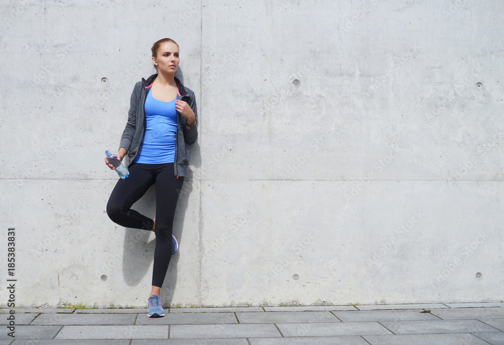 Young, fit and sporty woman standing in front of concrete cement wall. Fitness, sport, urban jogging and healthy lifestyle concept. Young, fit and sporty woman standing in front of concrete cement wall. Fitness, sport, urban jogging and healthy lifestyle concept.
