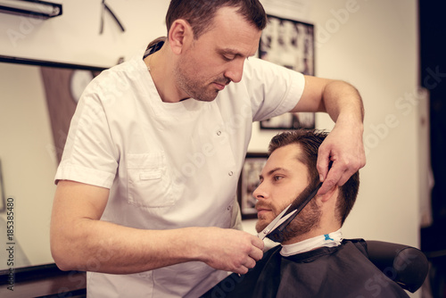 Professional barber cutting beard of handsome man