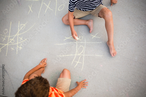 Two small boys chalking game of tic tac toe on driveway 