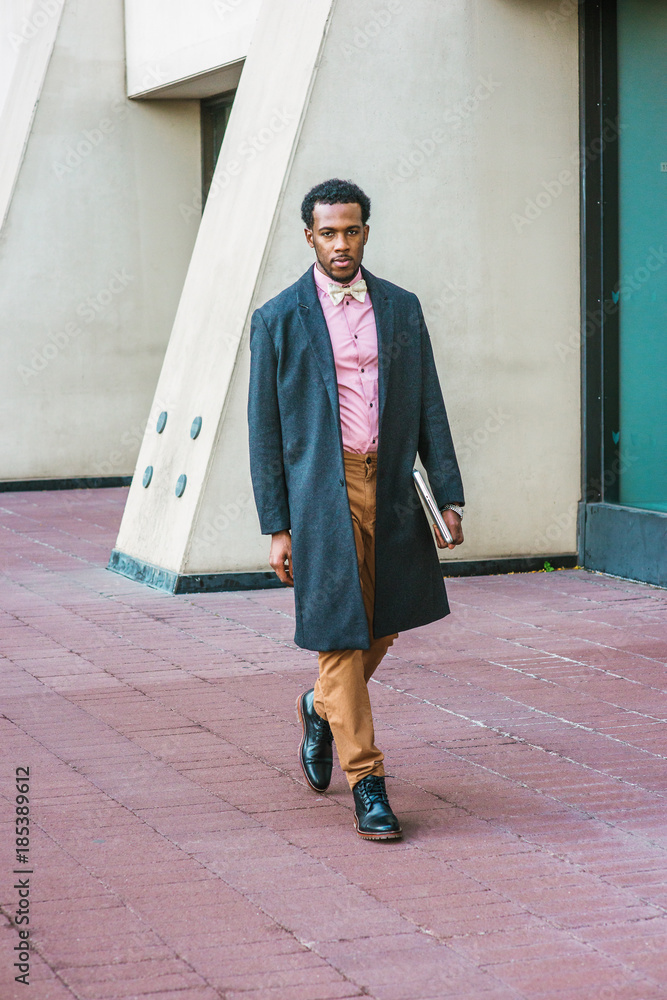 African American Business Man with beard traveling working in New York  wearing woolen overcoat pink shirt brown pants leather boot shoes bow  tie carrying laptop computer walking on street Stock Photo 