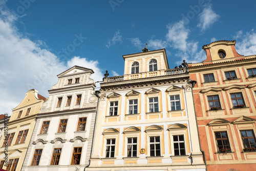 Row of vernacular houses surrounding Old Town Square in Prague  Czech Republic. Looking up at traditional historic architecture in Prague. Dutch gabled roof  dentils  and stone balcony. Blue skies.