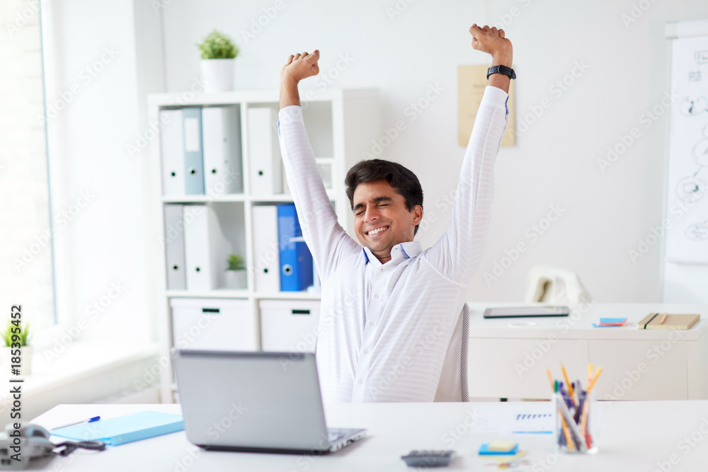 tired businessman with laptop stretching at office
